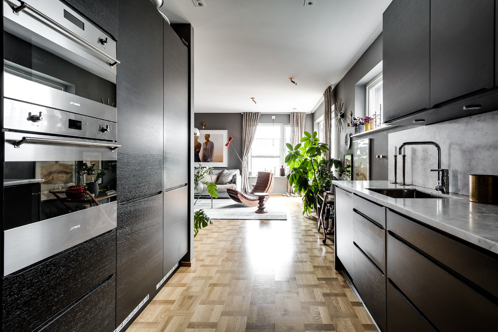 Ejemplo de cocinas en L escandinava grande abierta sin isla con fregadero encastrado, armarios con paneles lisos, encimera de mármol, salpicadero verde y suelo de madera en tonos medios