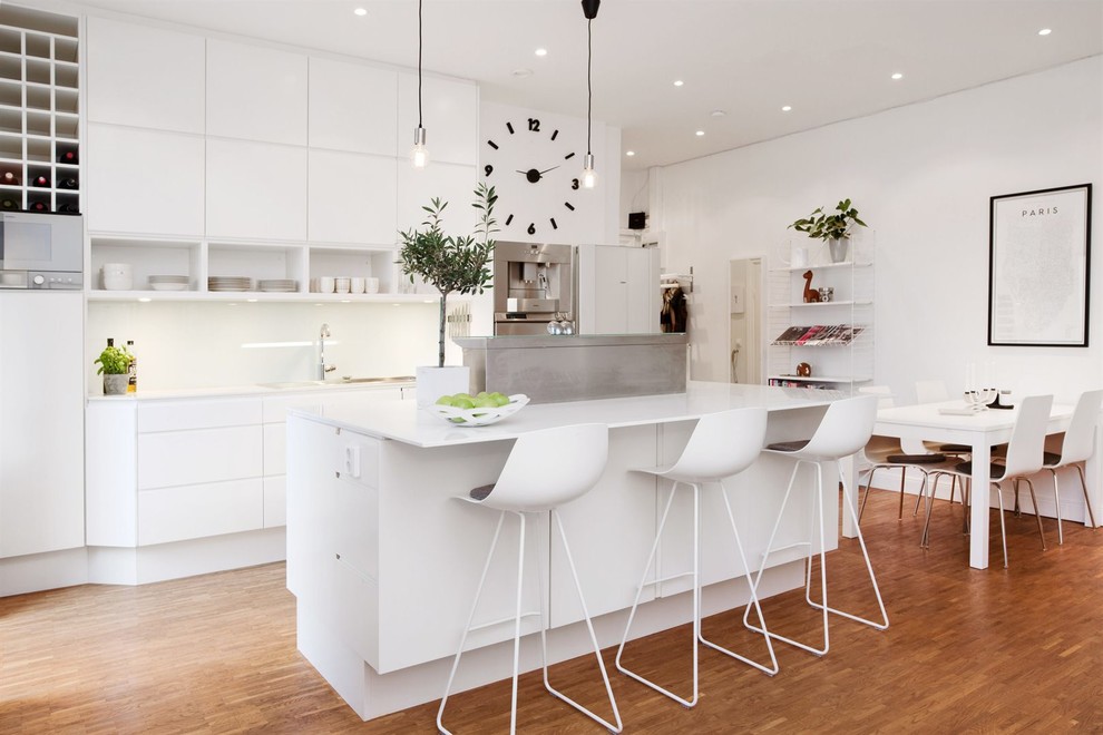 Foto på ett mellanstort minimalistiskt kök och matrum, med släta luckor, vita skåp, vitt stänkskydd, rostfria vitvaror, mellanmörkt trägolv och en köksö