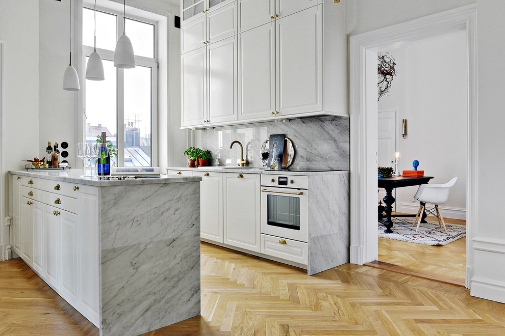 Nordisk inredning av ett mellanstort kök, med skåp i shakerstil, vita skåp, marmorbänkskiva, grått stänkskydd, vita vitvaror och ljust trägolv