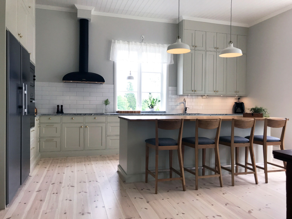 Bild på ett mycket stort lantligt grå grått l-kök, med en enkel diskho, skåp i shakerstil, gröna skåp, granitbänkskiva, vitt stänkskydd, stänkskydd i porslinskakel, rostfria vitvaror och en köksö