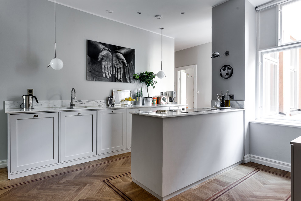 Modelo de cocina escandinava grande con fregadero bajoencimera, armarios estilo shaker, puertas de armario grises, electrodomésticos de acero inoxidable, suelo de madera clara y encimera de mármol