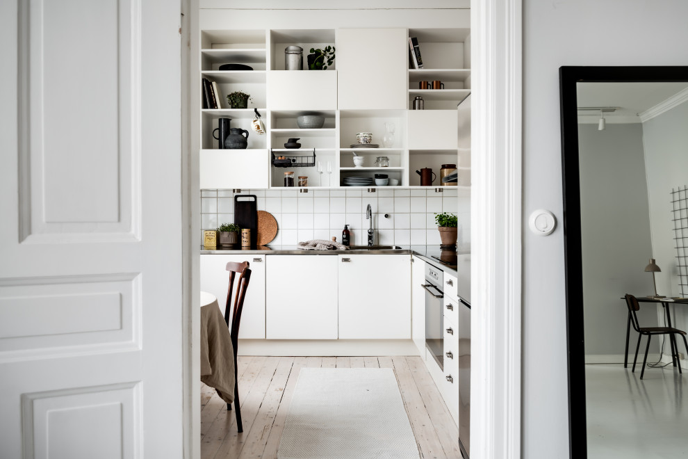 Danish l-shaped light wood floor and beige floor eat-in kitchen photo in Gothenburg with flat-panel cabinets, white cabinets, white backsplash, no island and gray countertops