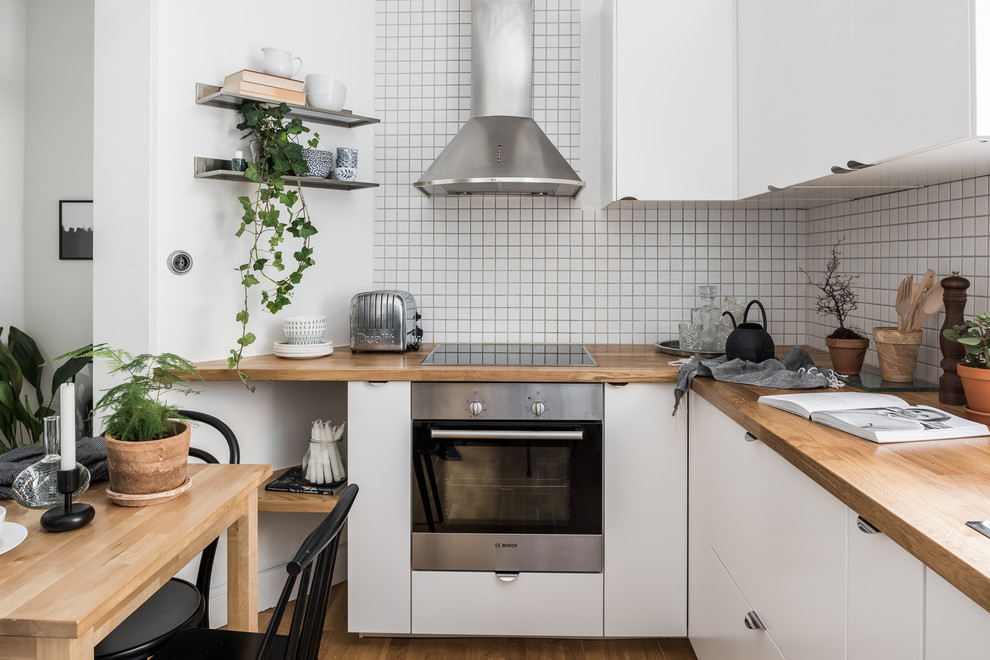 Foto på ett mellanstort nordiskt kök, med släta luckor, vita skåp, träbänkskiva, vitt stänkskydd och ljust trägolv