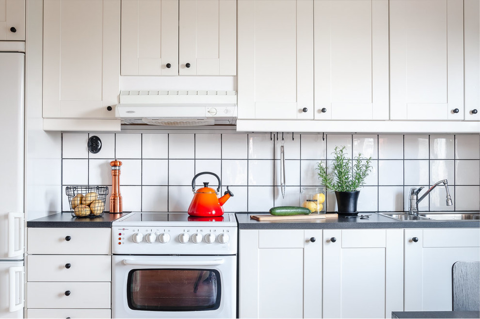 Nordisk inredning av ett mellanstort l-kök, med en nedsänkt diskho, skåp i shakerstil, vita skåp, vitt stänkskydd, stänkskydd i keramik och vita vitvaror