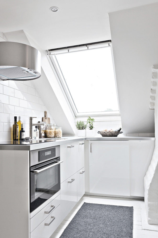 Nordisk inredning av ett mellanstort l-kök, med släta luckor, vita skåp, bänkskiva i rostfritt stål, vitt stänkskydd, stänkskydd i keramik, rostfria vitvaror och målat trägolv
