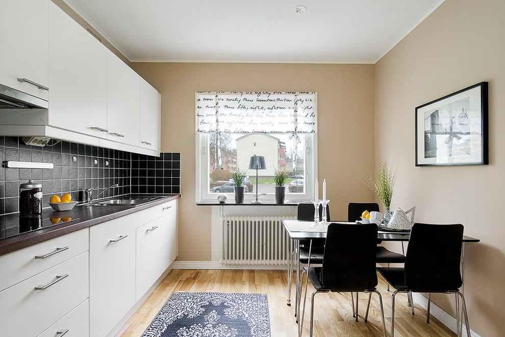 Inredning av ett minimalistiskt litet linjärt kök och matrum, med en nedsänkt diskho, släta luckor, vita skåp, svart stänkskydd, ljust trägolv, granitbänkskiva och vita vitvaror