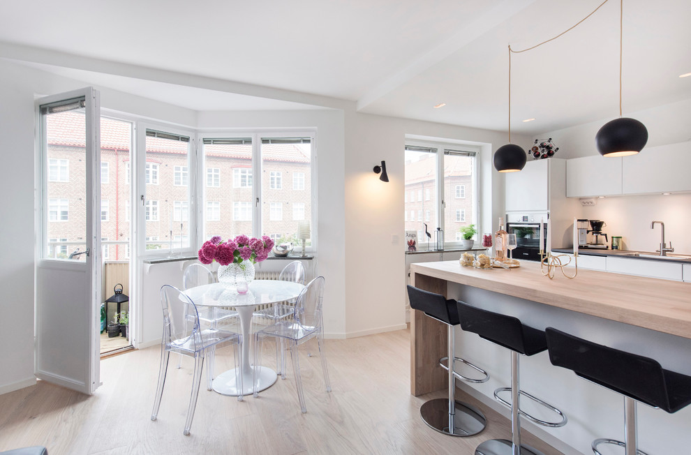 Eat-in kitchen - mid-sized scandinavian galley light wood floor eat-in kitchen idea in Malmo with a drop-in sink, flat-panel cabinets, white cabinets, wood countertops, stainless steel appliances and an island