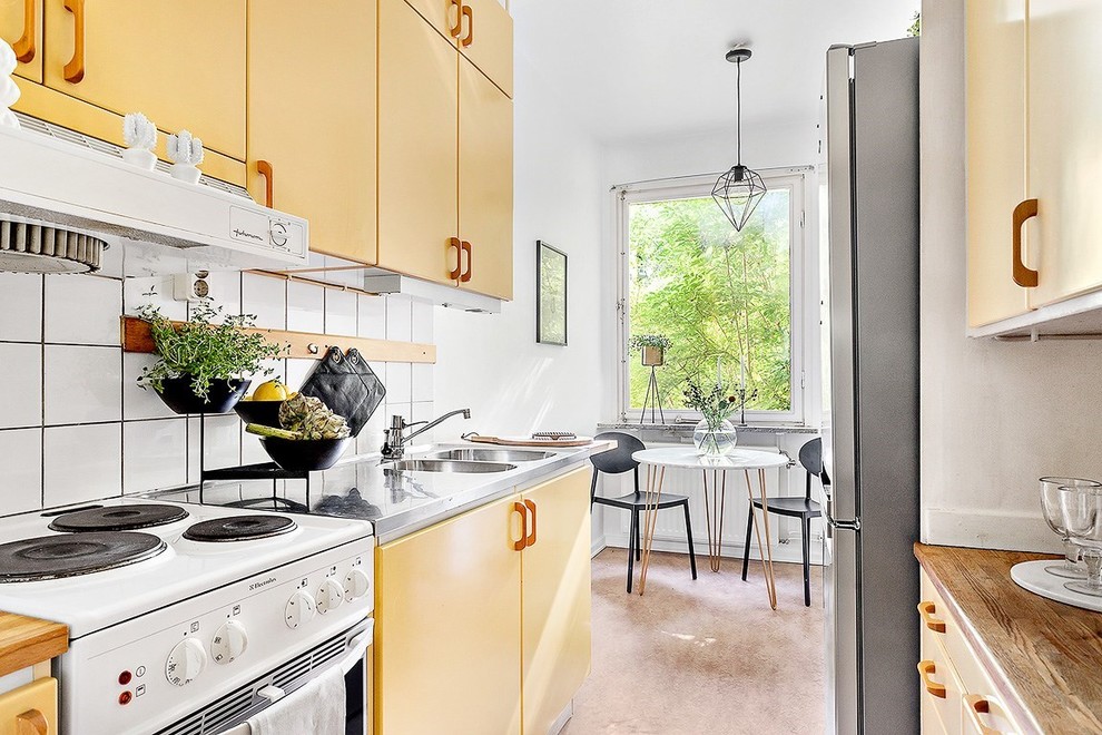 Foto på ett mellanstort minimalistiskt kök, med en dubbel diskho, släta luckor, gula skåp, bänkskiva i rostfritt stål, vitt stänkskydd, stänkskydd i keramik och vita vitvaror