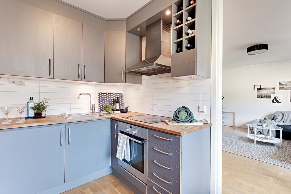 Exempel på ett minimalistiskt l-kök, med en nedsänkt diskho, släta luckor, grå skåp, vitt stänkskydd, ljust trägolv, träbänkskiva och rostfria vitvaror