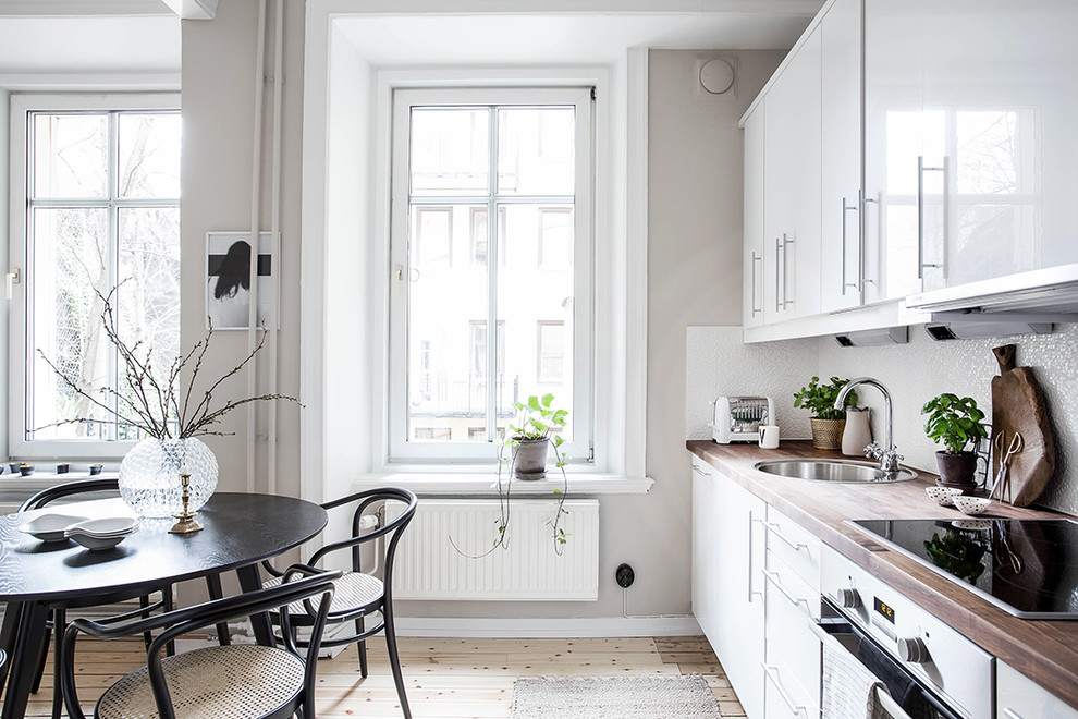 Foto på ett avskilt, mellanstort minimalistiskt linjärt kök, med ljust trägolv, en enkel diskho, släta luckor, vita skåp och träbänkskiva