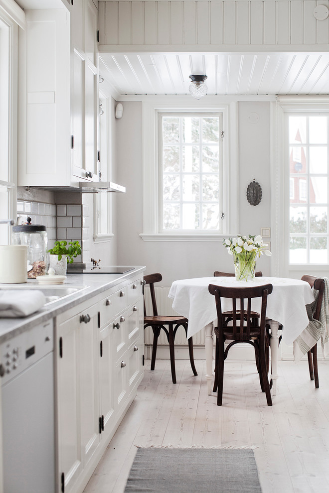 Design ideas for a medium sized farmhouse single-wall kitchen/diner in Stockholm with a double-bowl sink, recessed-panel cabinets, white cabinets, white splashback, metro tiled splashback, light hardwood flooring, marble worktops and no island.