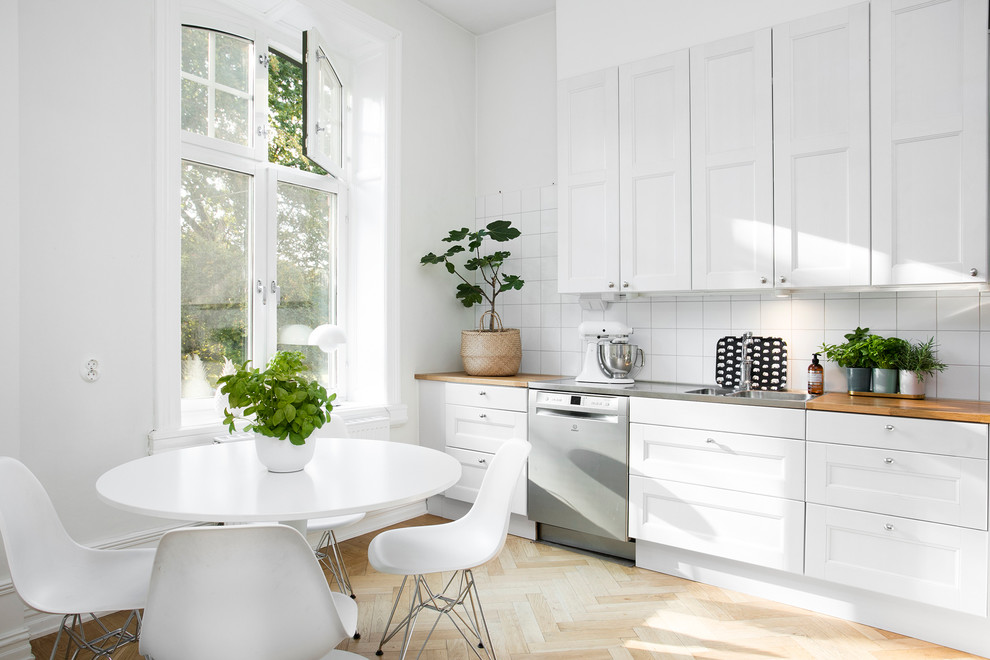 Exempel på ett mellanstort klassiskt linjärt kök och matrum, med en dubbel diskho, vita skåp, träbänkskiva, vitt stänkskydd, rostfria vitvaror, ljust trägolv och skåp i shakerstil