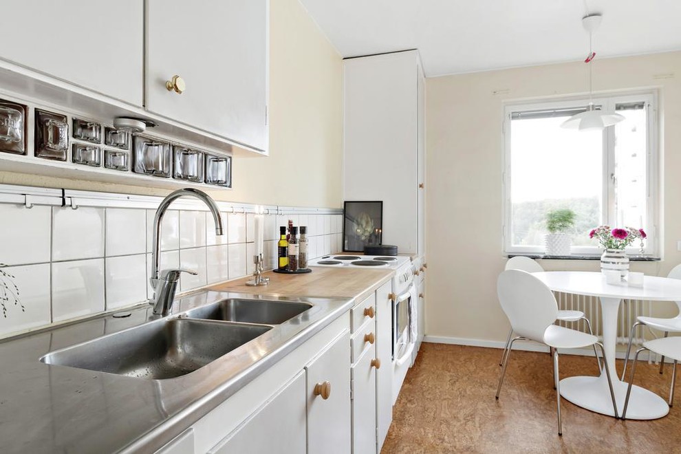 Immagine di una cucina scandinava con lavello a doppia vasca, ante lisce, ante bianche, top in legno, paraspruzzi bianco, elettrodomestici bianchi, pavimento marrone e top marrone