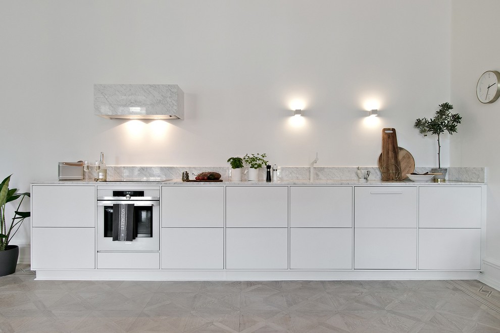 Inspiration for a scandinavian single-wall kitchen in Other with a submerged sink, flat-panel cabinets, white cabinets, grey splashback, white appliances, light hardwood flooring, no island, beige floors and grey worktops.