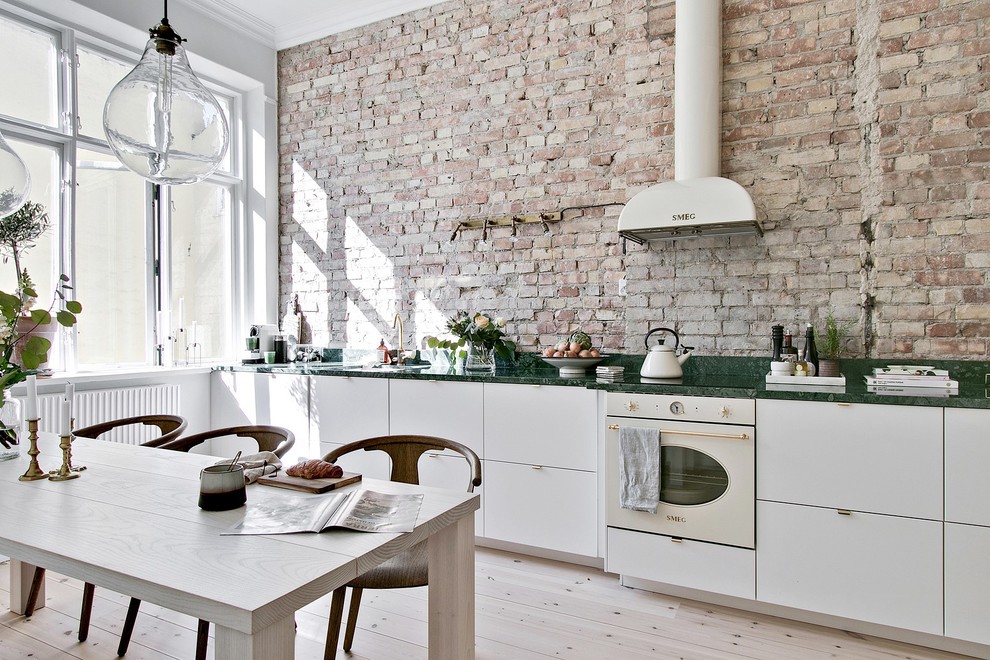 Inspiration for a large scandinavian single-wall light wood floor and beige floor eat-in kitchen remodel in Other with flat-panel cabinets, white cabinets, marble countertops, beige backsplash, brick backsplash, white appliances, no island and green countertops
