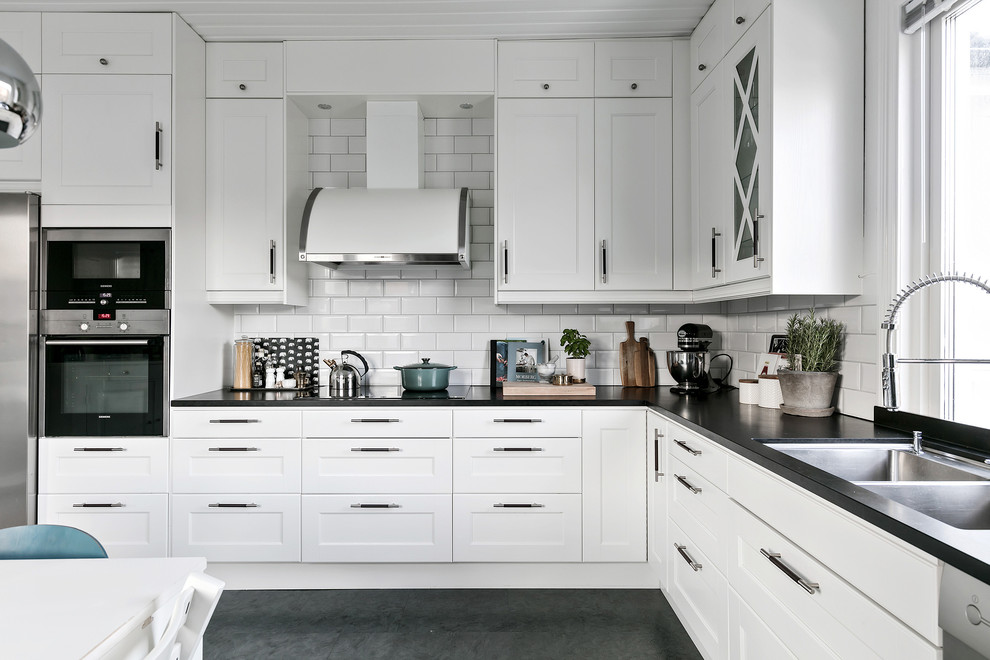 Foto di una cucina nordica con lavello a doppia vasca, ante con riquadro incassato, ante bianche, paraspruzzi bianco e elettrodomestici in acciaio inossidabile
