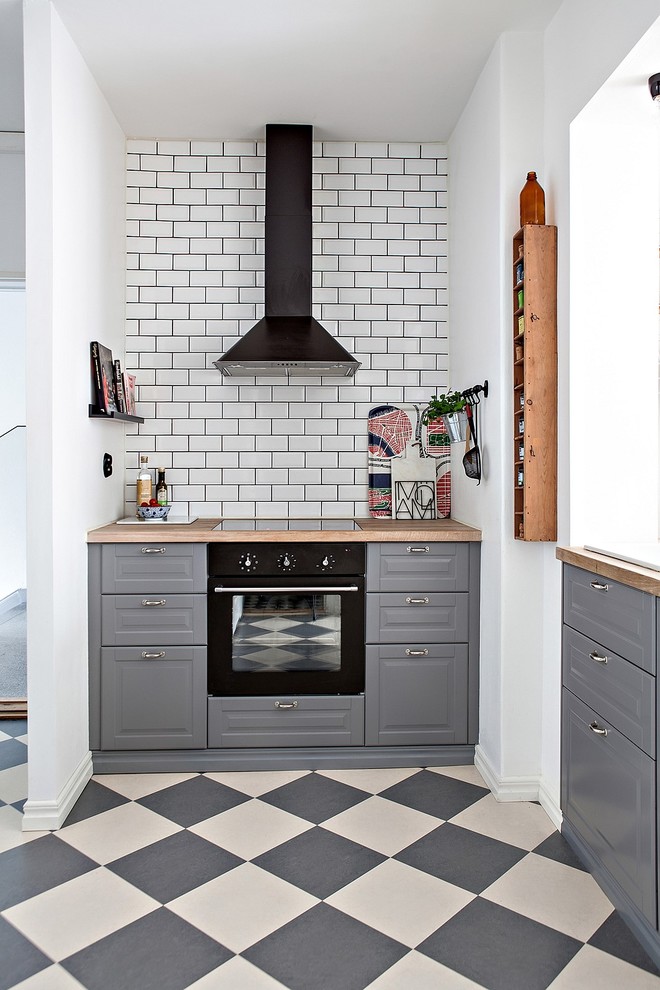 Foto på ett avskilt, litet nordiskt kök, med grå skåp, träbänkskiva, vitt stänkskydd, stänkskydd i tunnelbanekakel, svarta vitvaror, flerfärgat golv, linoleumgolv och luckor med upphöjd panel