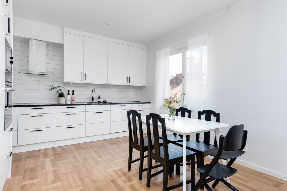 ストックホルムにある高級な中くらいな北欧スタイルのおしゃれなキッチン (フラットパネル扉のキャビネット、白いキッチンパネル、サブウェイタイルのキッチンパネル、淡色無垢フローリング、アイランドなし) の写真