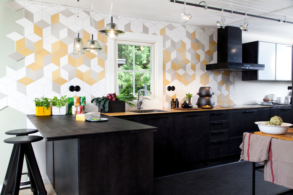 На фото: угловая кухня среднего размера в скандинавском стиле с врезной мойкой, разноцветным фартуком, полуостровом, плоскими фасадами, черными фасадами и деревянной столешницей с