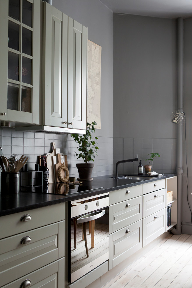 Idéer för ett mellanstort minimalistiskt linjärt kök och matrum, med en nedsänkt diskho, gröna skåp, grått stänkskydd, rostfria vitvaror, ljust trägolv och luckor med upphöjd panel