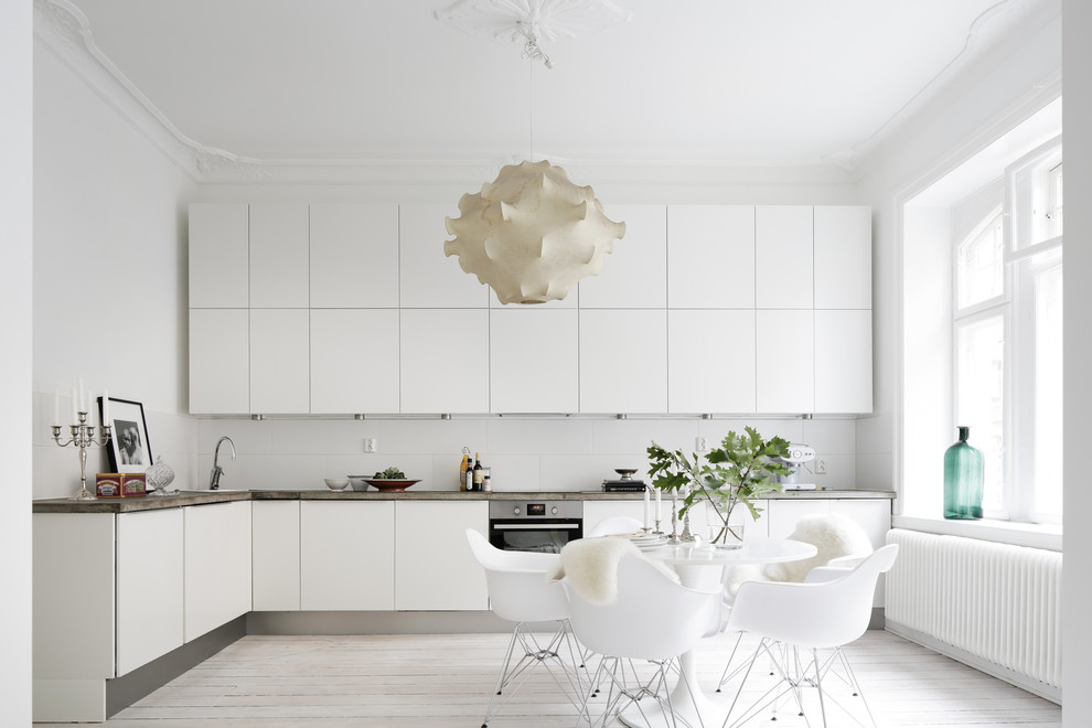 Mittelgroße Skandinavische Küche ohne Insel in L-Form mit flächenbündigen Schrankfronten, weißen Schränken, Küchenrückwand in Weiß, Küchengeräten aus Edelstahl und gebeiztem Holzboden in Malmö