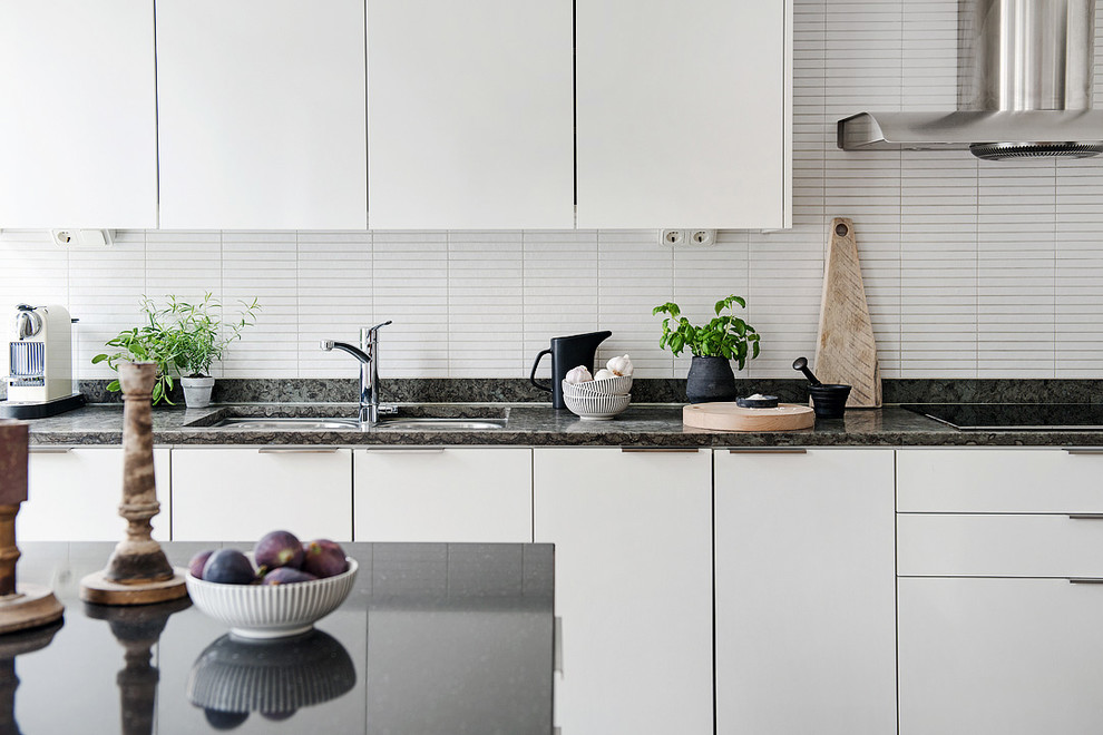 Zweizeilige, Geschlossene Nordische Küche mit flächenbündigen Schrankfronten, weißen Schränken, Küchenrückwand in Weiß, Küchengeräten aus Edelstahl, Kücheninsel, Doppelwaschbecken und Granit-Arbeitsplatte in Göteborg