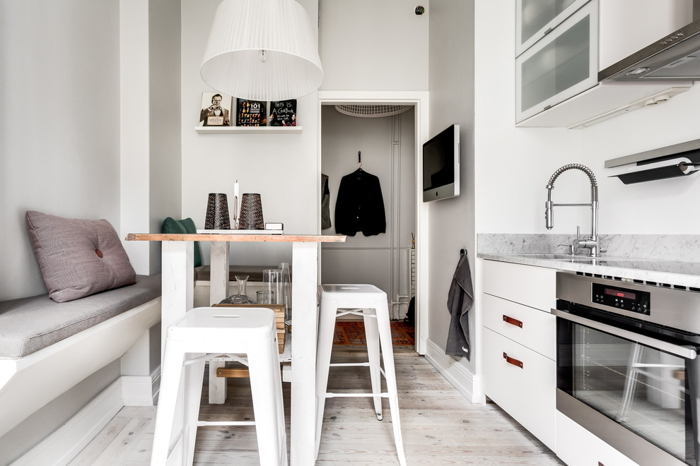ストックホルムにある高級な小さな北欧スタイルのおしゃれなキッチン (フラットパネル扉のキャビネット、白いキャビネット、大理石カウンター、白いキッチンパネル、シルバーの調理設備、アイランドなし) の写真