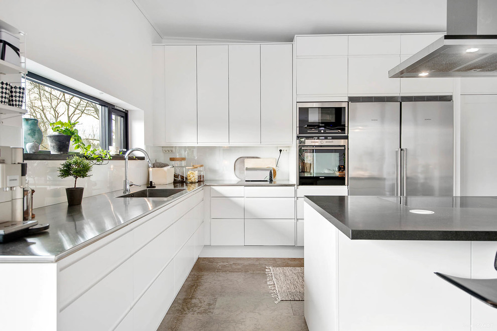 Foto på ett minimalistiskt l-kök, med släta luckor, vita skåp, vitt stänkskydd, rostfria vitvaror och en köksö