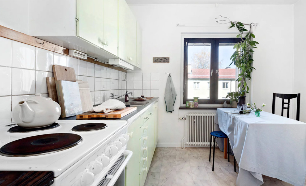 Midcentury single-wall kitchen/diner in Stockholm with a double-bowl sink, flat-panel cabinets, green cabinets, stainless steel worktops, white splashback, porcelain splashback, white appliances, vinyl flooring and multi-coloured floors.