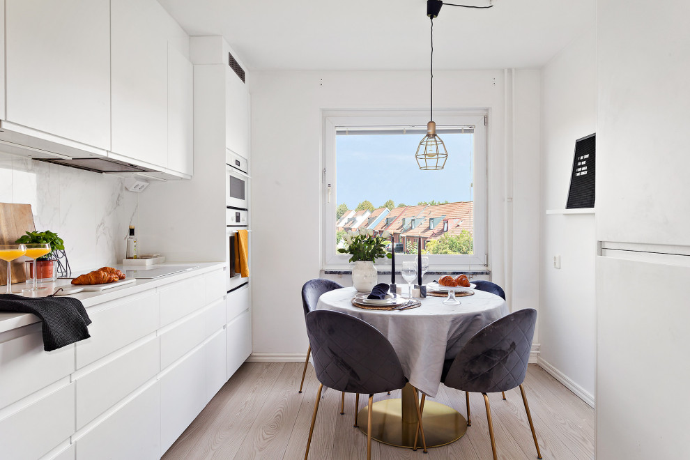 Foto på ett minimalistiskt vit linjärt kök och matrum, med släta luckor, vita skåp, vitt stänkskydd, stänkskydd i sten, vita vitvaror, ljust trägolv och beiget golv