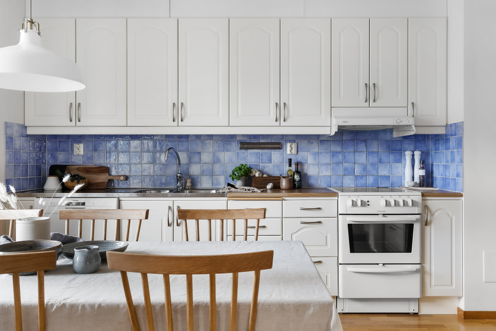Inspiration för nordiska linjära brunt kök och matrum, med en integrerad diskho, luckor med upphöjd panel, vita skåp, träbänkskiva, blått stänkskydd, vita vitvaror, mellanmörkt trägolv och brunt golv