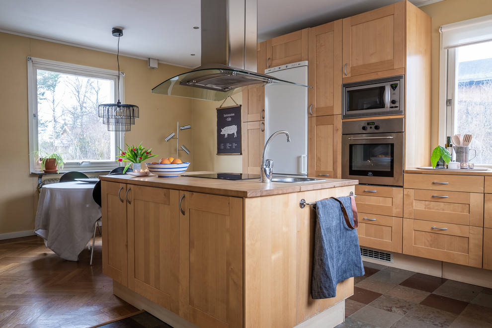 Bild på ett minimalistiskt kök och matrum, med en enkel diskho, luckor med infälld panel, skåp i ljust trä, träbänkskiva, rostfria vitvaror, en köksö och flerfärgat golv
