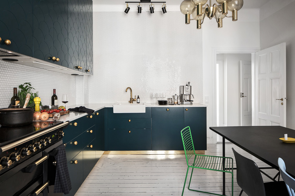 Minimalistisk inredning av ett stort kök, med en rustik diskho, släta luckor, blå skåp, vitt stänkskydd, ljust trägolv, marmorbänkskiva och svarta vitvaror