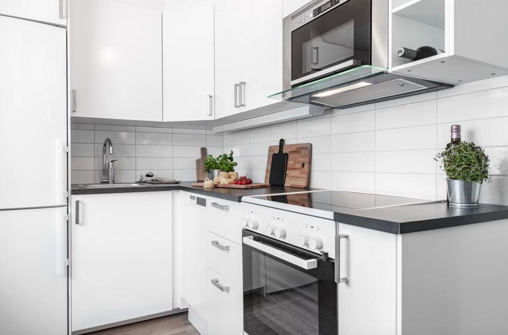 Nordisk inredning av ett litet kök, med en enkel diskho, släta luckor, vita skåp, laminatbänkskiva, vitt stänkskydd, stänkskydd i porslinskakel, vita vitvaror, ljust trägolv och beiget golv