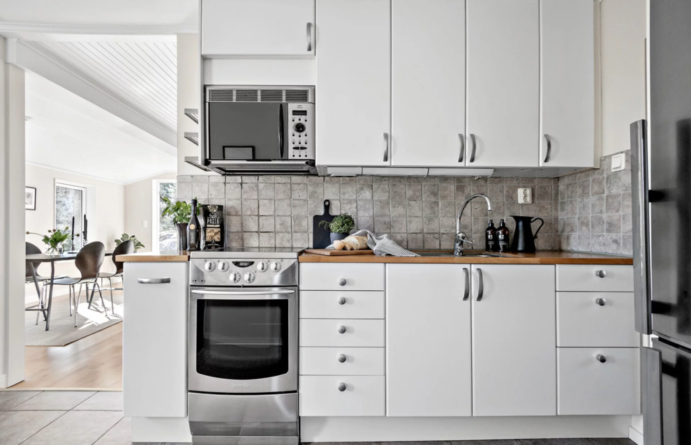 Photo of a small scandi single-wall kitchen/diner in Stockholm with a double-bowl sink, flat-panel cabinets, white cabinets, wood worktops, multi-coloured splashback, stone tiled splashback, stainless steel appliances, slate flooring, multi-coloured floors and beige worktops.
