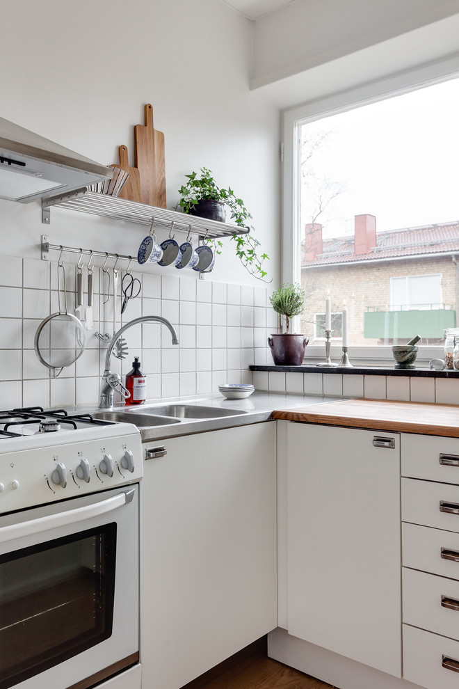 Foto de cocinas en L escandinava, de tamaño medio, cerrada, sin isla, con fregadero de doble seno, armarios con paneles lisos, puertas de armario blancas, encimera de madera, salpicadero blanco y electrodomésticos blancos