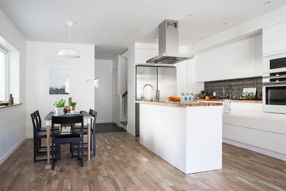 Minimalistisk inredning av ett mellanstort linjärt kök och matrum, med släta luckor, vita skåp, träbänkskiva, svart stänkskydd och en köksö