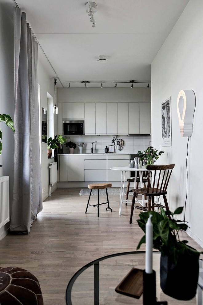 Inredning av ett minimalistiskt linjärt kök och matrum, med släta luckor, grå skåp, vitt stänkskydd, rostfria vitvaror, ljust trägolv och beiget golv