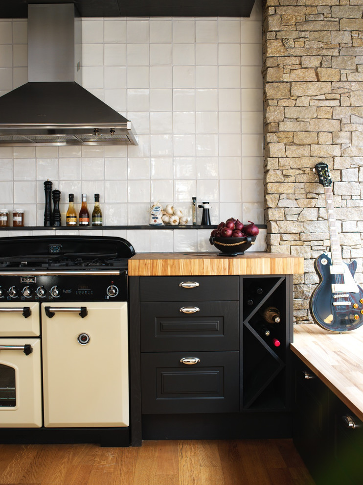 This is an example of a rustic single-wall kitchen in Malmo with raised-panel cabinets, black cabinets, wood worktops, black splashback, white appliances, medium hardwood flooring and no island.
