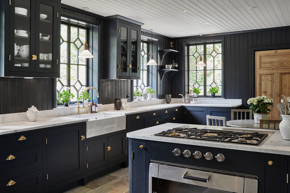 Photo of a large farmhouse l-shaped kitchen/diner in Stockholm with a belfast sink, shaker cabinets, blue cabinets, marble worktops, black splashback, stainless steel appliances, an island and ceramic flooring.