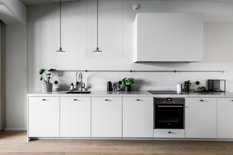 Minimalistisk inredning av ett mellanstort linjärt kök med öppen planlösning, med en enkel diskho, släta luckor, vita skåp, marmorbänkskiva, vitt stänkskydd, rostfria vitvaror, mellanmörkt trägolv och brunt golv