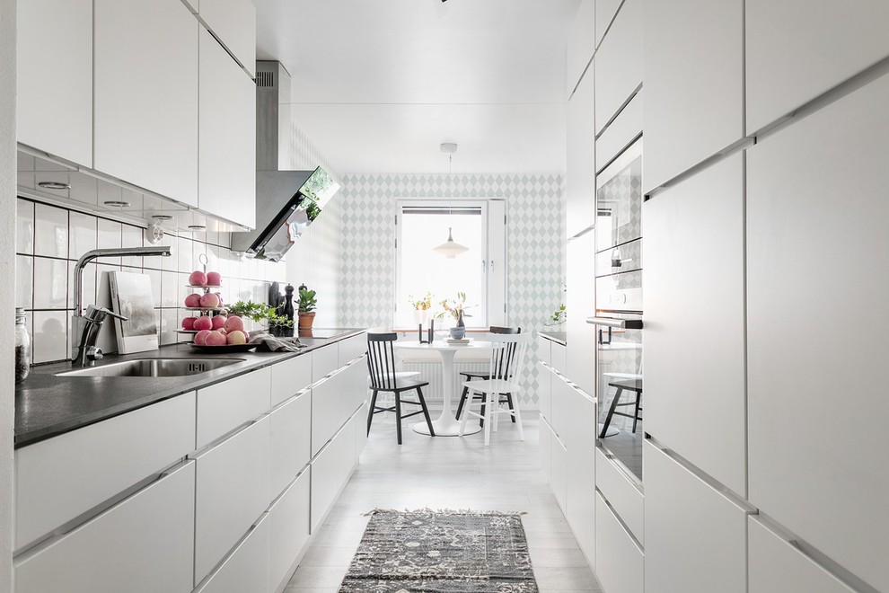 Идея дизайна: параллельная кухня в скандинавском стиле с обеденным столом, плоскими фасадами, врезной мойкой, белыми фасадами, белым фартуком, белым полом, деревянным полом и обоями на стенах