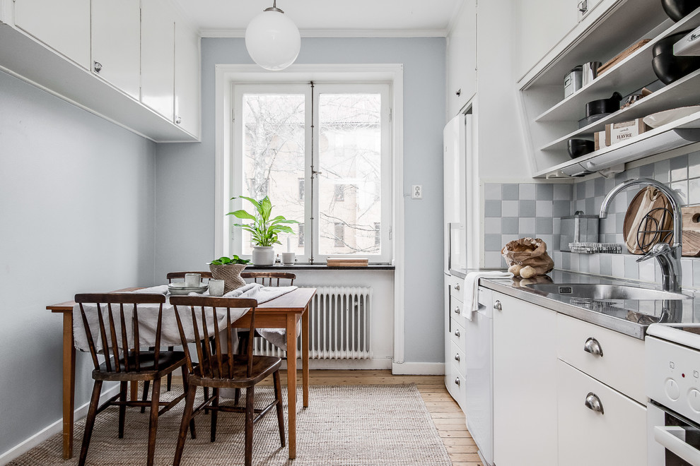 Foto på ett 60 tals grå linjärt kök och matrum, med en integrerad diskho, släta luckor, vita skåp, bänkskiva i rostfritt stål, flerfärgad stänkskydd, vita vitvaror, ljust trägolv och beiget golv