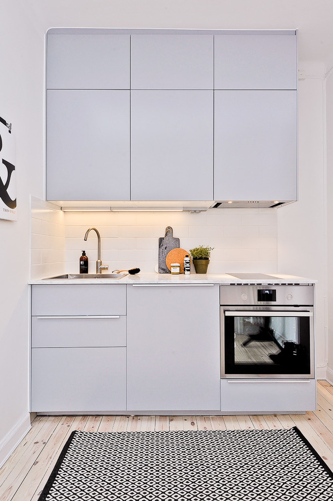 Foto på ett litet nordiskt linjärt kök, med släta luckor, grå skåp, marmorbänkskiva, grått stänkskydd, rostfria vitvaror, ljust trägolv och en nedsänkt diskho