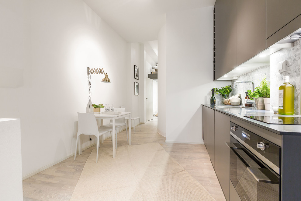 This is an example of a scandi single-wall kitchen/diner in Stockholm with flat-panel cabinets, grey cabinets, grey splashback, mosaic tiled splashback, light hardwood flooring, no island, a single-bowl sink and stainless steel appliances.