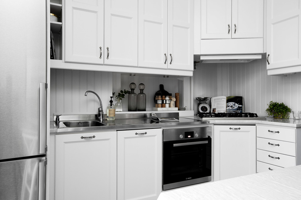 Ejemplo de cocinas en U escandinavo con fregadero integrado, armarios con paneles empotrados, puertas de armario blancas, encimera de acero inoxidable y electrodomésticos de acero inoxidable
