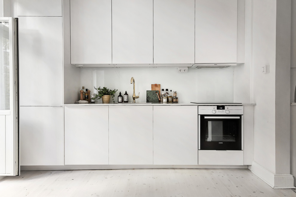Inspiration för ett mellanstort skandinaviskt linjärt kök, med en enkel diskho, släta luckor, vita skåp, laminatbänkskiva, vita vitvaror och ljust trägolv