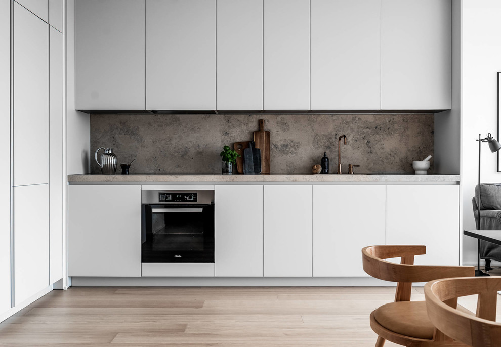 Inspiration for a contemporary l-shaped open plan kitchen in Stockholm with flat-panel cabinets, white cabinets, grey splashback, stone slab splashback, light hardwood flooring, no island, beige floors and grey worktops.