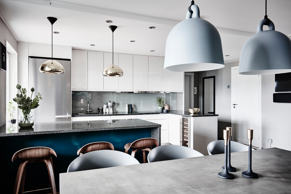 Foto på ett funkis kök och matrum, med släta luckor, vita skåp, granitbänkskiva, blått stänkskydd, glaspanel som stänkskydd, rostfria vitvaror och en köksö