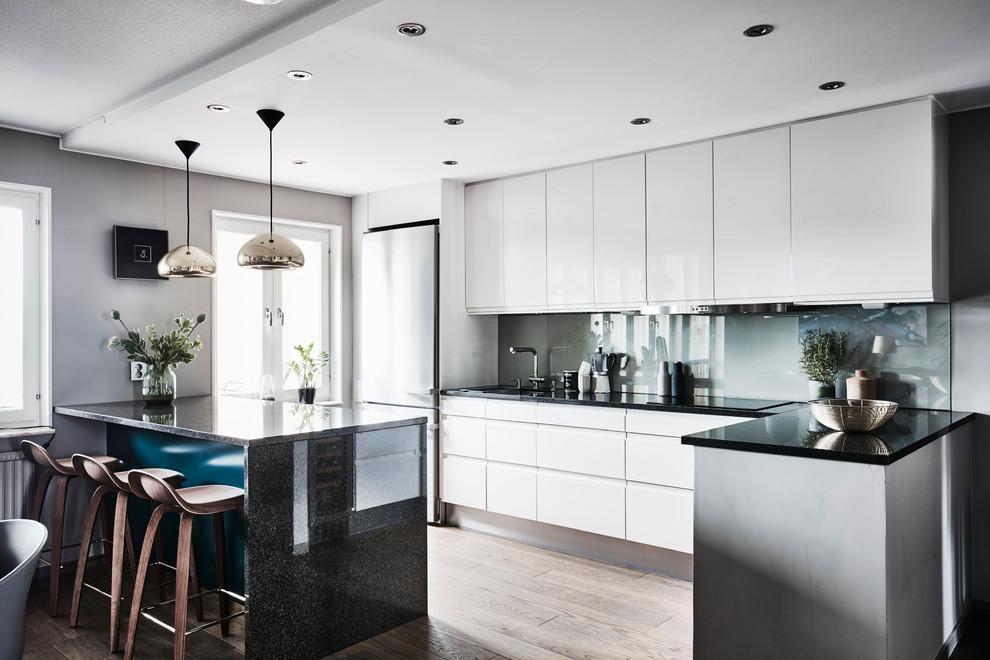 Einzeilige, Mittelgroße Moderne Küche mit flächenbündigen Schrankfronten, weißen Schränken, Granit-Arbeitsplatte, hellem Holzboden, Küchenrückwand in Blau, Glasrückwand und beigem Boden in Göteborg
